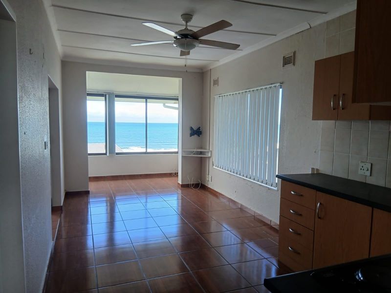 Open-plan living and kitchen area featuring tiled floors, built-in cabinetry, and expansive ocean views through large windows.