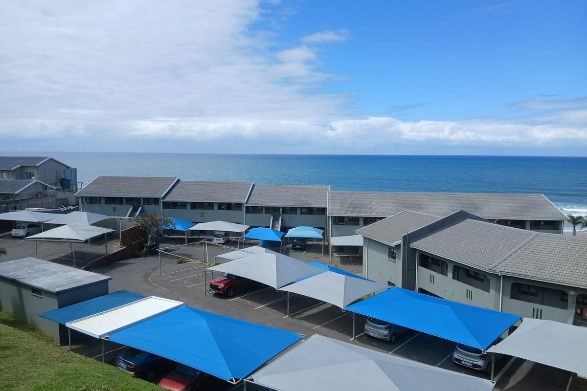 An elevated aerial view of the apartment complex grounds, featuring multiple covered parking bays and proximity to the coastline.