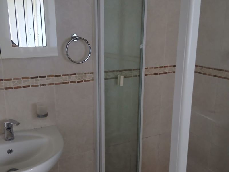 A functional bathroom featuring a pedestal basin, a shower enclosure with tiled flooring, and neutral wall tiling with a decorative border.