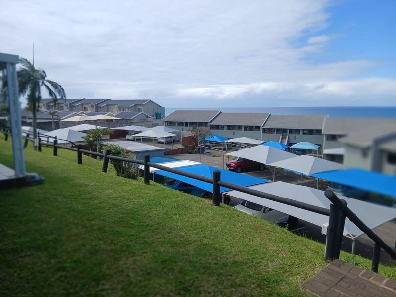 Elevated view overlooking the apartment complex parking area with shade structures and distant ocean horizon.