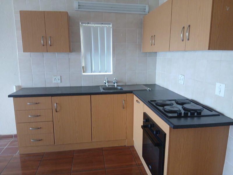 A functional kitchen featuring laminate cabinetry, built-in oven, electric hob, tiled backsplash, and durable tiled flooring.