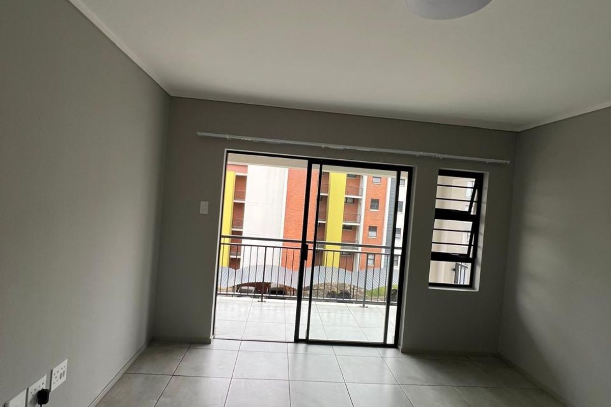 An empty, well-maintained living area featuring neutral tiled flooring, a sliding glass door leading to a balcony, and modern finishes.