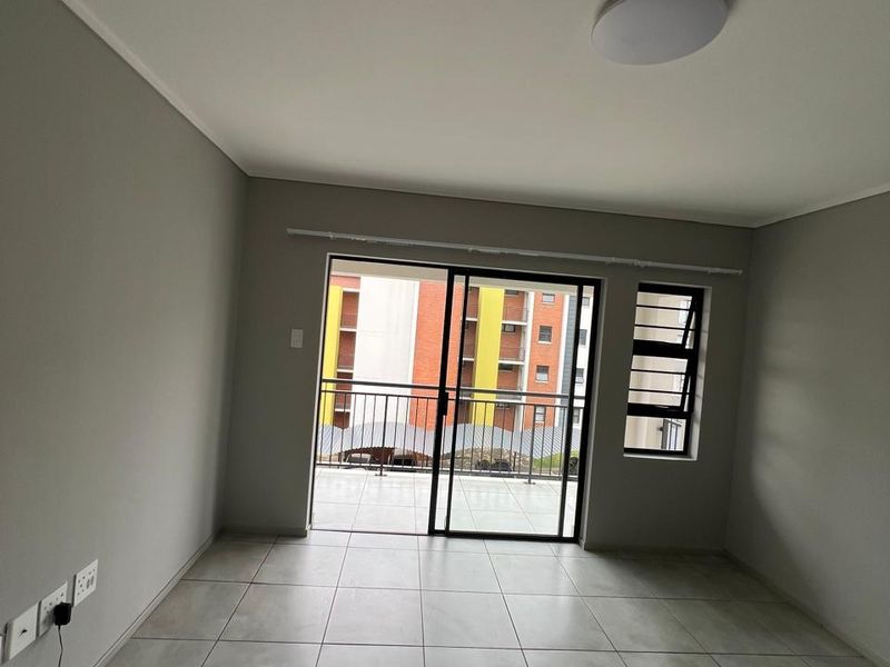 An empty, well-maintained living area featuring neutral tiled flooring, a sliding glass door leading to a balcony, and modern finishes.