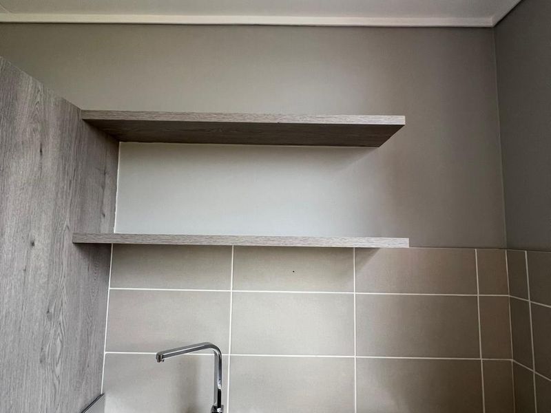A clean and modern kitchen area featuring a stainless steel double sink, chrome mixer tap, tiled splashback, and convenient floating shelving.