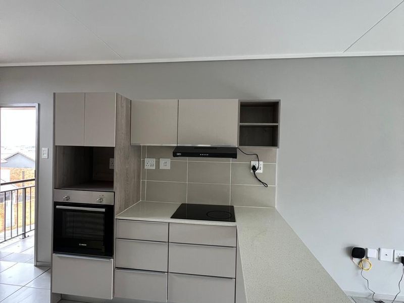 Modern open-plan kitchen featuring sleek laminate cabinetry, stone countertops, built-in oven, electric hob, and extractor fan, with neutral tiled flooring throughout.