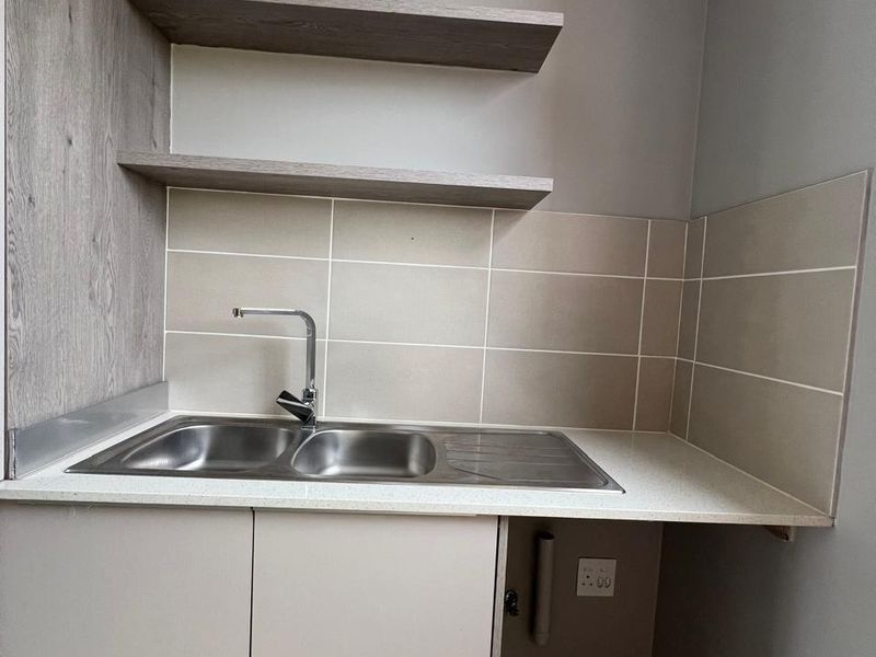 A clean and functional laundry area featuring a stainless steel double sink, stone countertop, tiled splashback, and convenient floating shelving for storage.