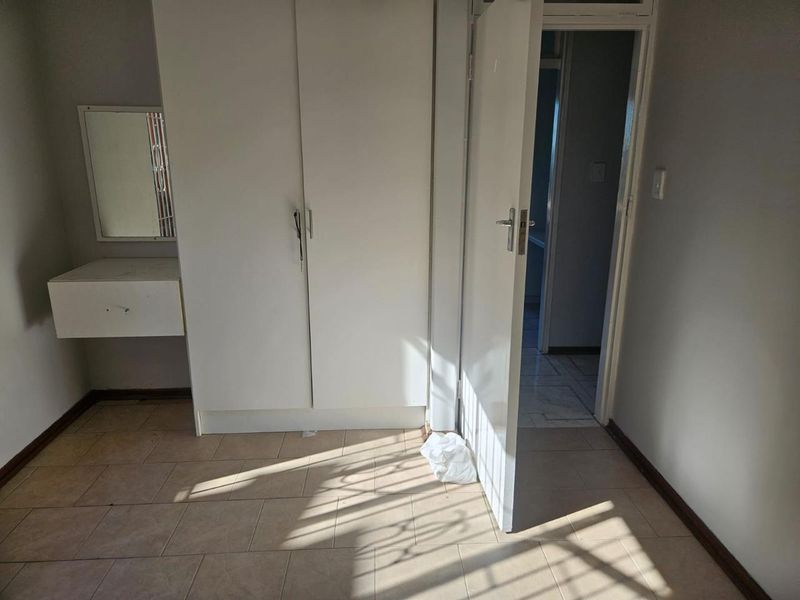 An empty bedroom featuring built-in cupboards, a wall-mounted vanity unit, and tiled flooring, with direct access to an adjoining room.