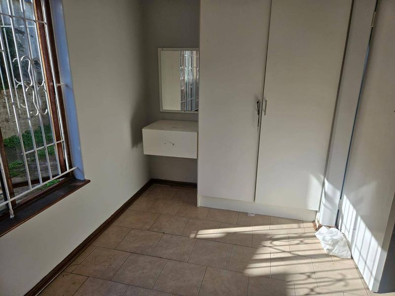 A compact bedroom featuring built-in wardrobe storage, a wall-mounted vanity unit, tiled flooring, and security bars on the window.