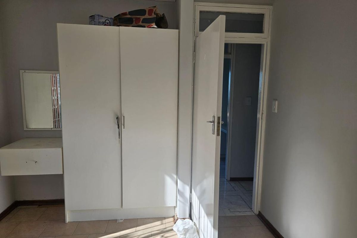 A bedroom featuring a built-in wardrobe, integrated vanity unit, and tiled flooring, with a doorway leading to an adjacent room.