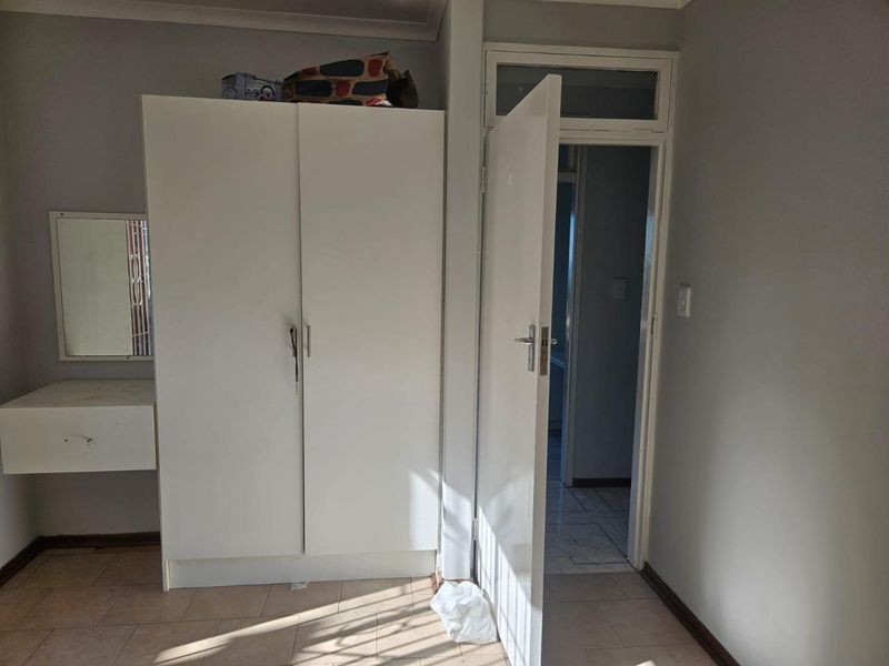 A bedroom featuring a built-in wardrobe, integrated vanity unit, and tiled flooring, with a doorway leading to an adjacent room.