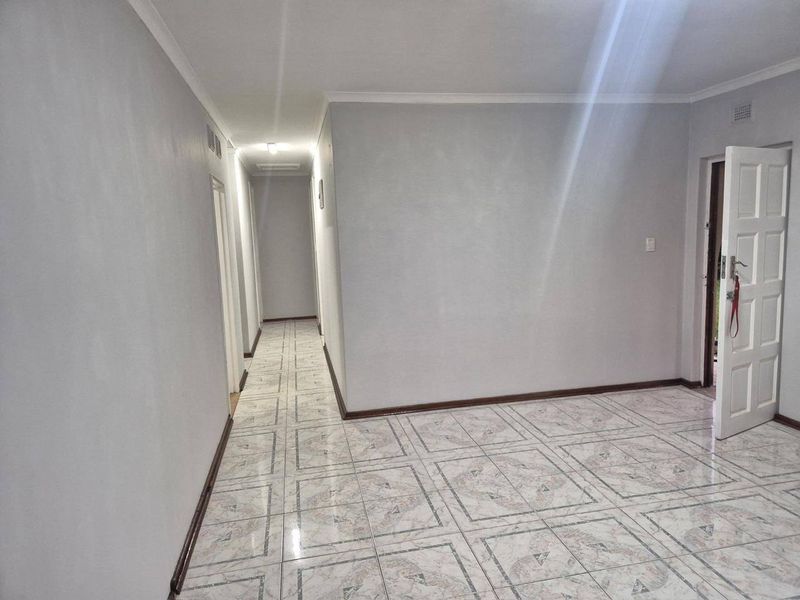 A clean, empty hallway featuring neutral wall paint, tiled flooring, and a classic panelled door leading to adjacent rooms.