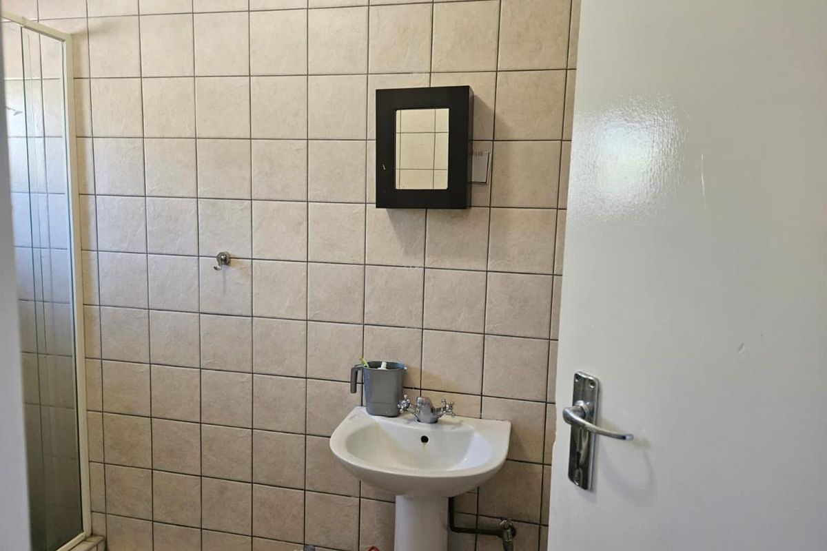 A functional bathroom featuring a pedestal basin, shower enclosure, and neutral ceramic wall tiling throughout.