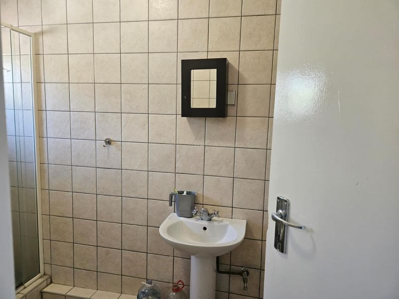 A functional bathroom featuring a pedestal basin, shower enclosure, and neutral ceramic wall tiling throughout.