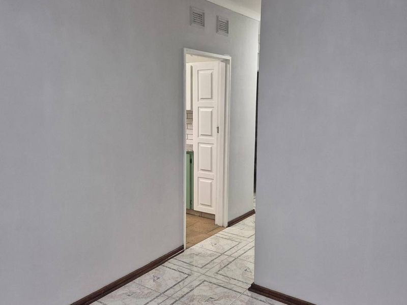 A clean, empty hallway featuring neutral wall paint, tiled flooring, and coving, providing access to adjacent rooms.