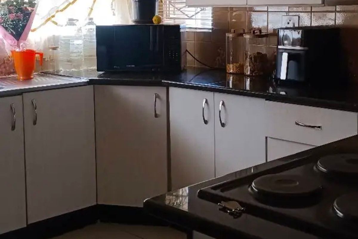 A functional kitchen featuring white cabinetry, dark granite countertops, tiled backsplash, and a built-in electric hob with ceramic floor tiles.
