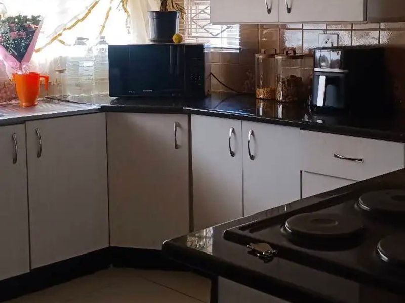A functional kitchen featuring white cabinetry, dark granite countertops, tiled backsplash, and a built-in electric hob with ceramic floor tiles.