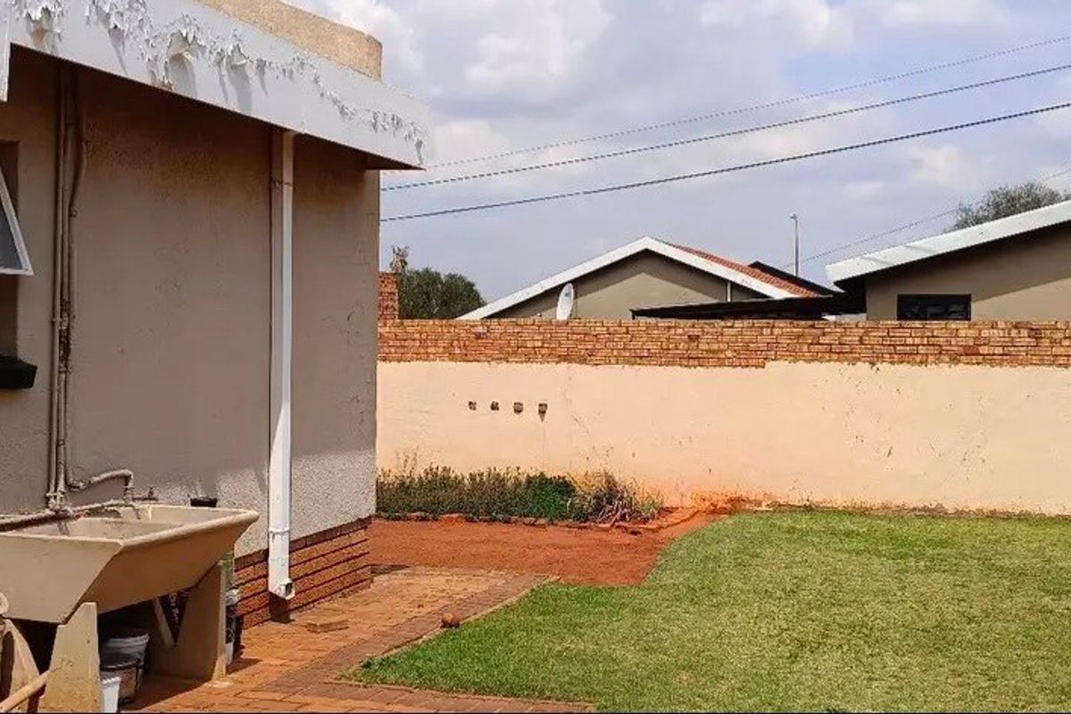 Rear exterior view showing a small garden, paved walkway, brick boundary wall, and a fixed concrete laundry trough attached to the house wall.