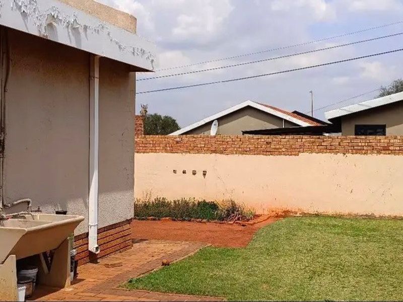Rear exterior view showing a small garden, paved walkway, brick boundary wall, and a fixed concrete laundry trough attached to the house wall.