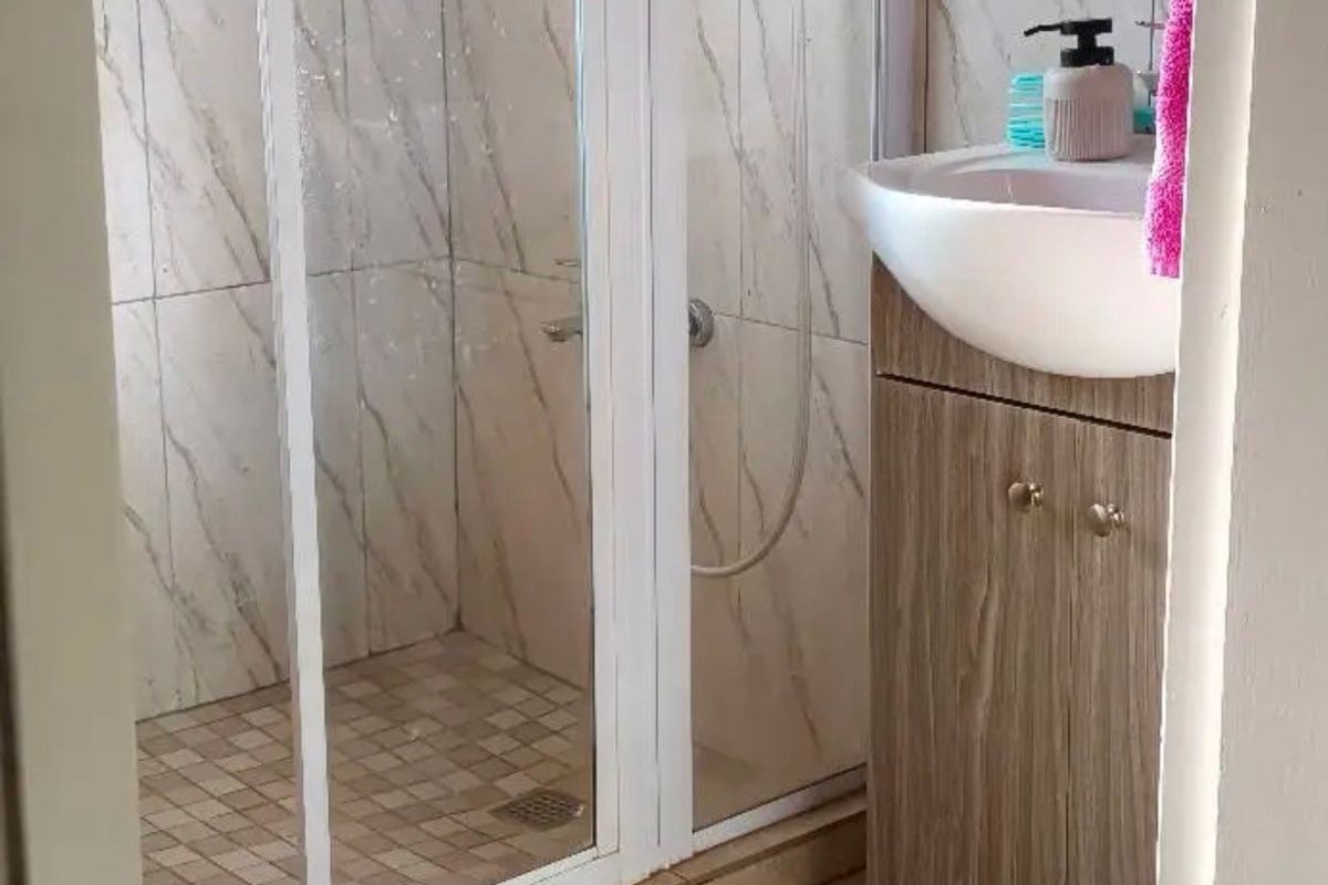 A compact bathroom featuring a shower enclosure with marble-look wall tiles, a vanity cabinet with a basin, and tiled flooring.