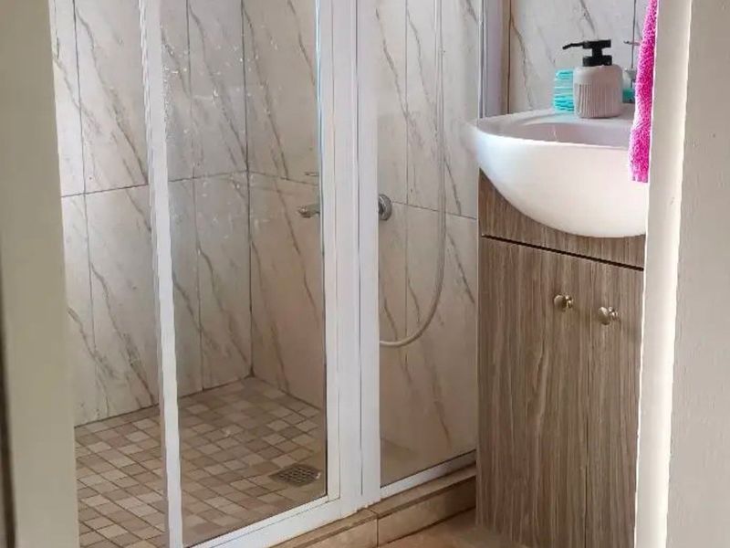 A compact bathroom featuring a shower enclosure with marble-look wall tiles, a vanity cabinet with a basin, and tiled flooring.