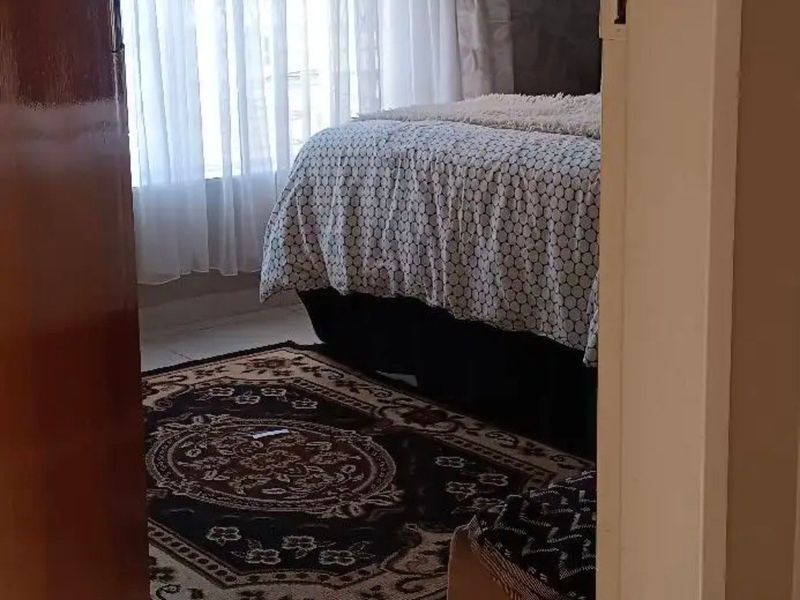 A bedroom featuring tiled flooring and natural light through window curtains, viewed from the doorway.
