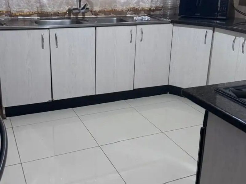 A functional kitchen featuring white laminate cabinetry, dark granite countertops, a double basin sink, and light-colored floor tiles.