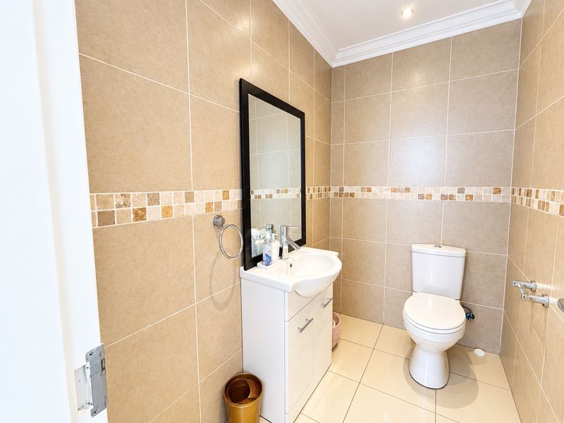 A well-maintained bathroom featuring neutral ceramic wall and floor tiles, a modern vanity unit with basin, and a wall-mounted mirror.