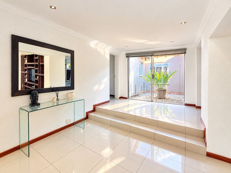 A bright and modern entrance hall featuring polished tiled flooring, recessed downlighting, and a sliding glass door providing access to a private courtyard.