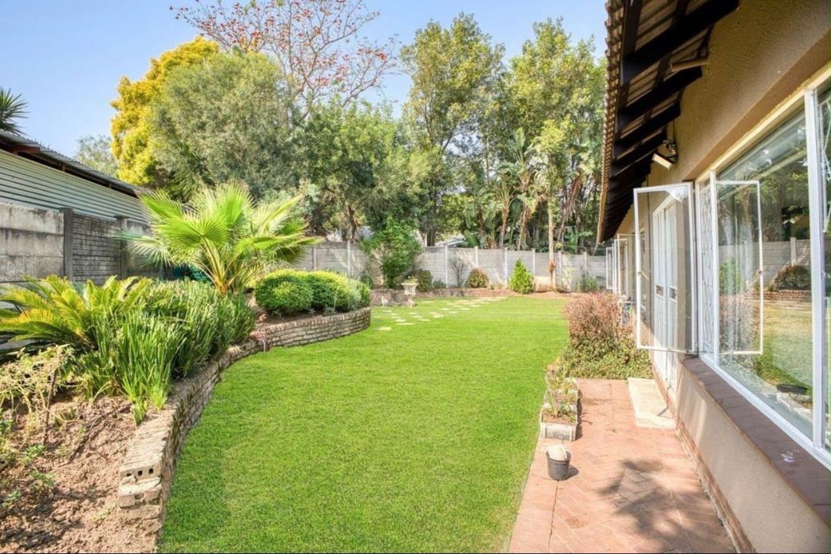 A well-maintained rear garden featuring a lush lawn, brick retaining walls, and a paved walkway adjacent to the house.