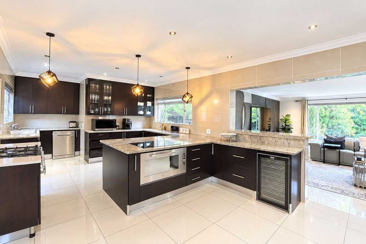 Modern open-plan kitchen featuring dark cabinetry, granite countertops, high-end built-in appliances, and polished tile flooring, seamlessly connecting to the adjacent living area.
