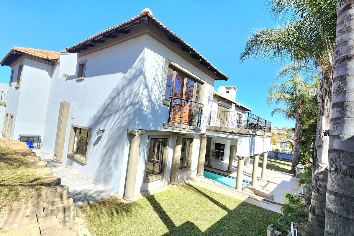 Rear view of the property featuring a swimming pool, paved patio area, and an elevated balcony with wrought iron railings.