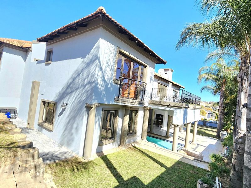 Rear view of the property featuring a swimming pool, paved patio area, and an elevated balcony with wrought iron railings.