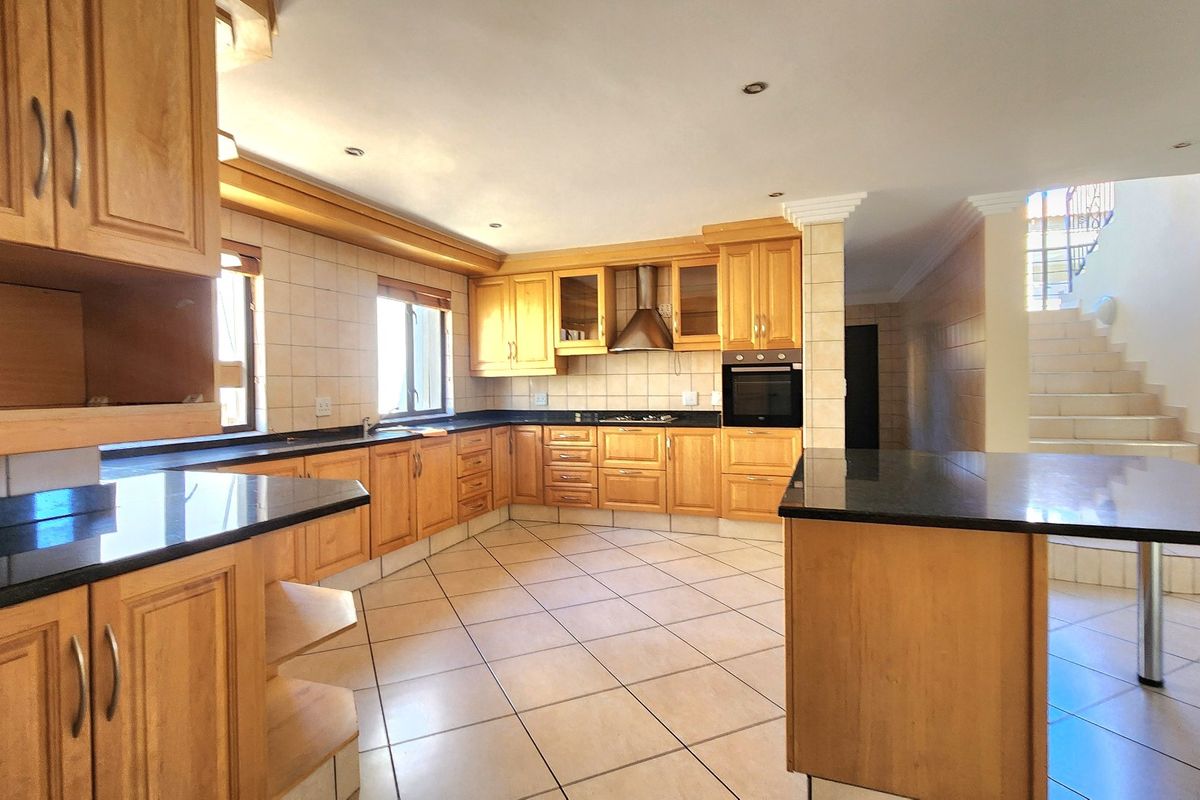 Spacious kitchen featuring wooden cabinetry, granite countertops, built-in oven, extractor fan, and tiled flooring, offering a functional layout with ample storage space.