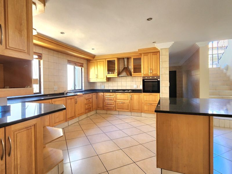 Spacious kitchen featuring wooden cabinetry, granite countertops, built-in oven, extractor fan, and tiled flooring, offering a functional layout with ample storage space.