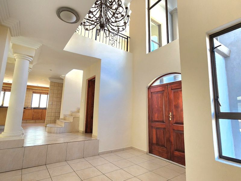 Spacious double-volume entrance hall featuring tiled flooring, a grand chandelier, and a staircase leading to the upper level.