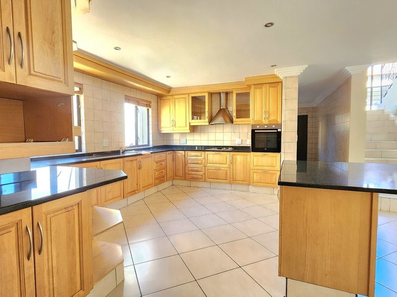 Spacious kitchen featuring extensive wooden cabinetry, granite countertops, built-in oven, stainless steel extractor fan, and tiled flooring with an integrated island.