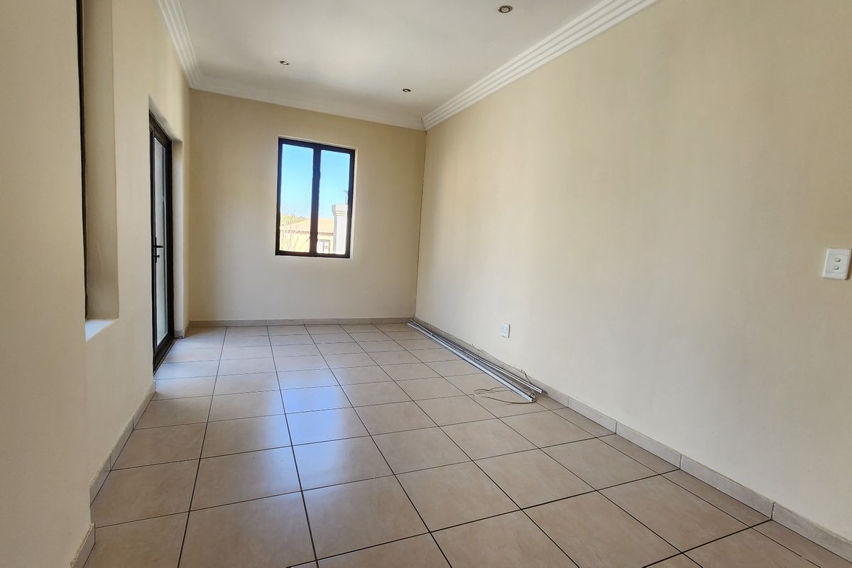 An empty bedroom featuring neutral tiled flooring, recessed downlighting, cornicing, and access to an outdoor area via a sliding door.