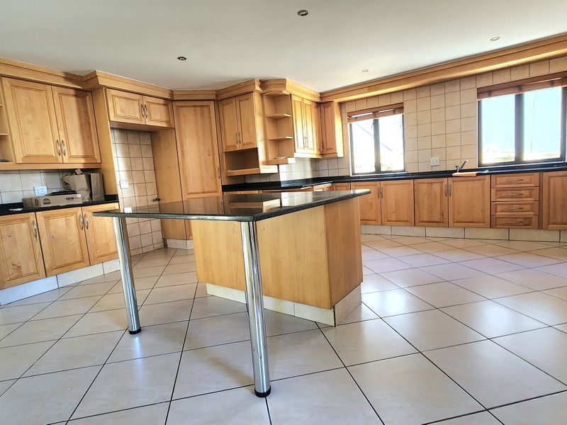 Spacious kitchen featuring extensive wooden cabinetry, granite countertops, a central island, and neutral tiled flooring throughout.