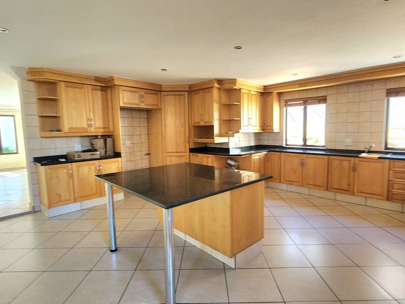 Spacious kitchen featuring light wood cabinetry, granite countertops, a central island, and tiled flooring throughout.