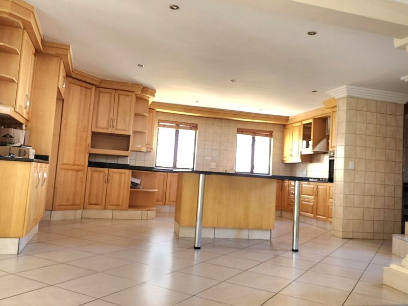 Spacious kitchen featuring light wood cabinetry, granite countertops, a central island, and tiled flooring, offering a functional layout with ample storage space.