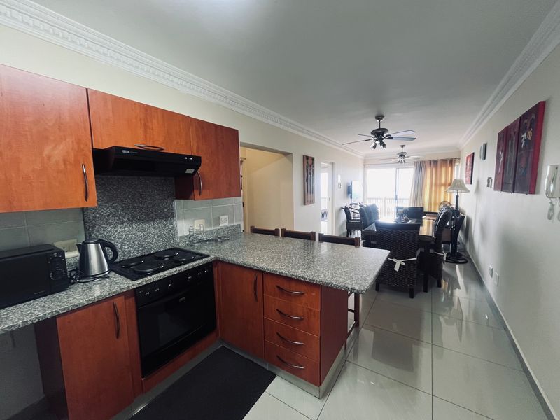 Open-plan kitchen and dining area featuring granite countertops, wooden cabinetry, built-in appliances, and tiled flooring leading to a balcony.