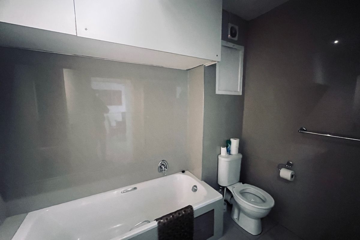 A functional bathroom featuring a bathtub, toilet, and wall-mounted cabinetry with neutral wall finishes.