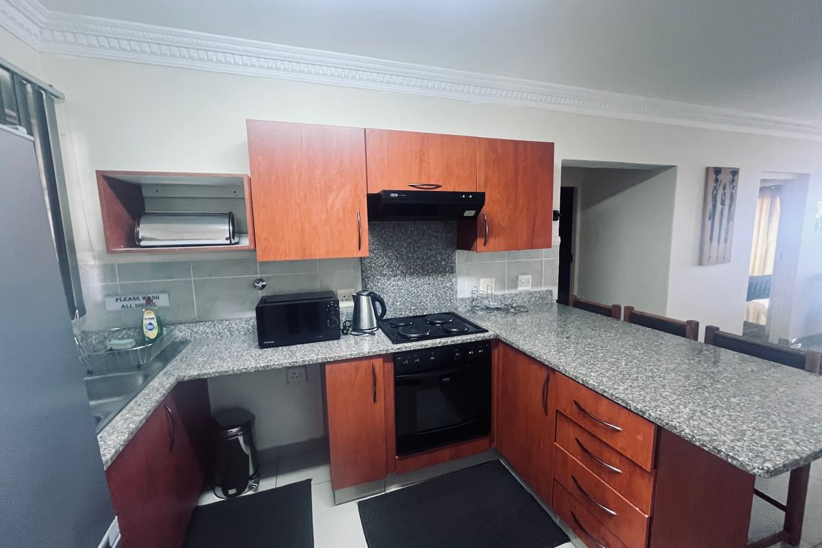A functional kitchen featuring granite countertops, wooden cabinetry, built-in oven, electric hob, and an extractor fan with a tiled backsplash.