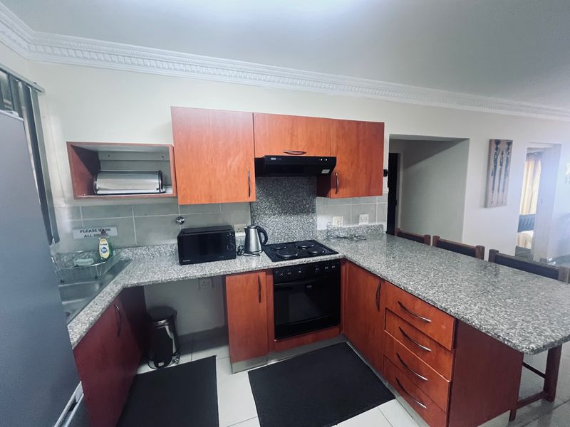 A functional kitchen featuring granite countertops, wooden cabinetry, built-in oven, electric hob, and an extractor fan with a tiled backsplash.