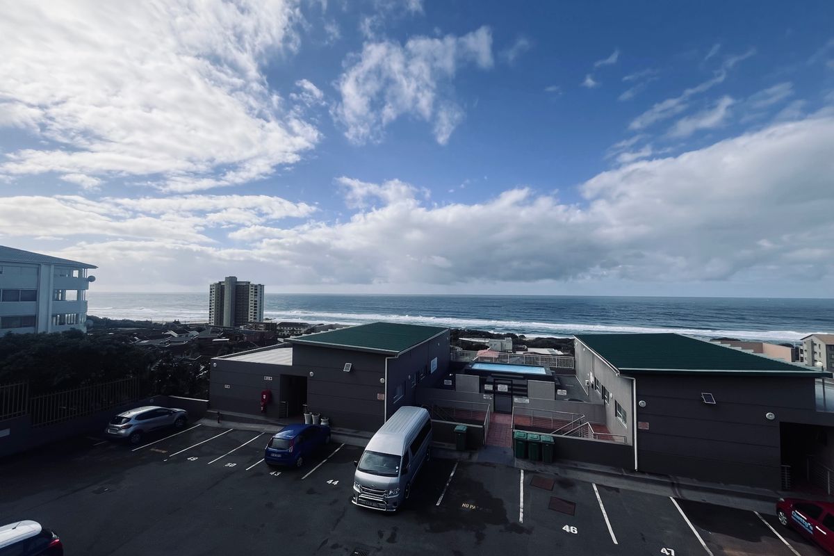 Aerial view of the apartment complex parking area and swimming pool, featuring ocean views in the background.