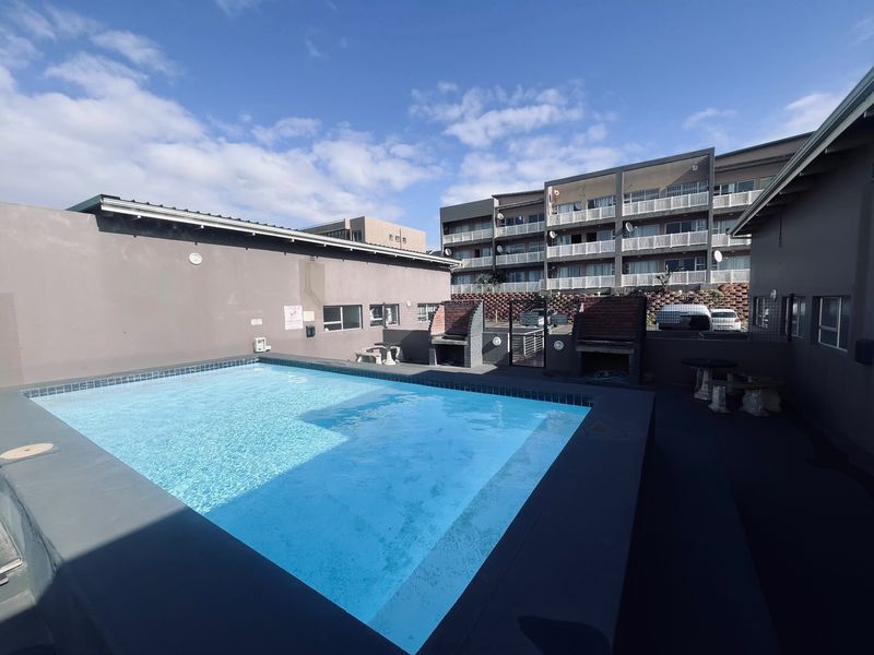 Communal pool area featuring a swimming pool and built-in braai facilities, set within a paved courtyard of the apartment complex.