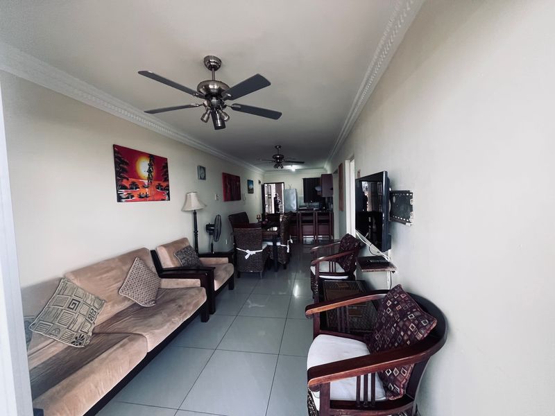 Open-plan living and dining area featuring tiled flooring, crown molding, and ceiling fans, flowing into a functional kitchen space.