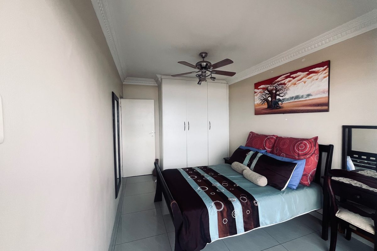 A well-maintained bedroom featuring built-in cupboards, a ceiling fan, and tiled flooring with decorative cornice detailing.
