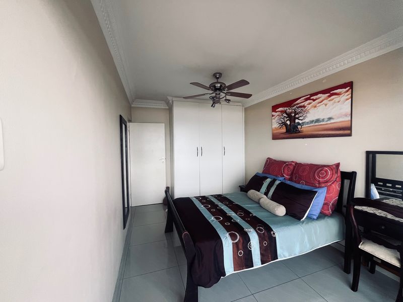 A well-maintained bedroom featuring built-in cupboards, a ceiling fan, and tiled flooring with decorative cornice detailing.