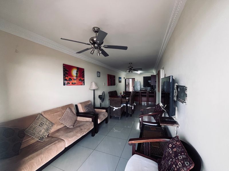 An open-plan living and dining area featuring tiled floors, crown molding, ceiling fans, and a connected kitchen space with a breakfast bar.